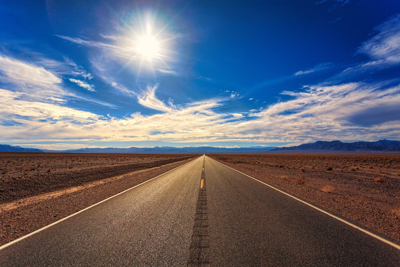 Eine lange Straße, die den Weg zeigt und blauer Himmel mit Sonnenschein